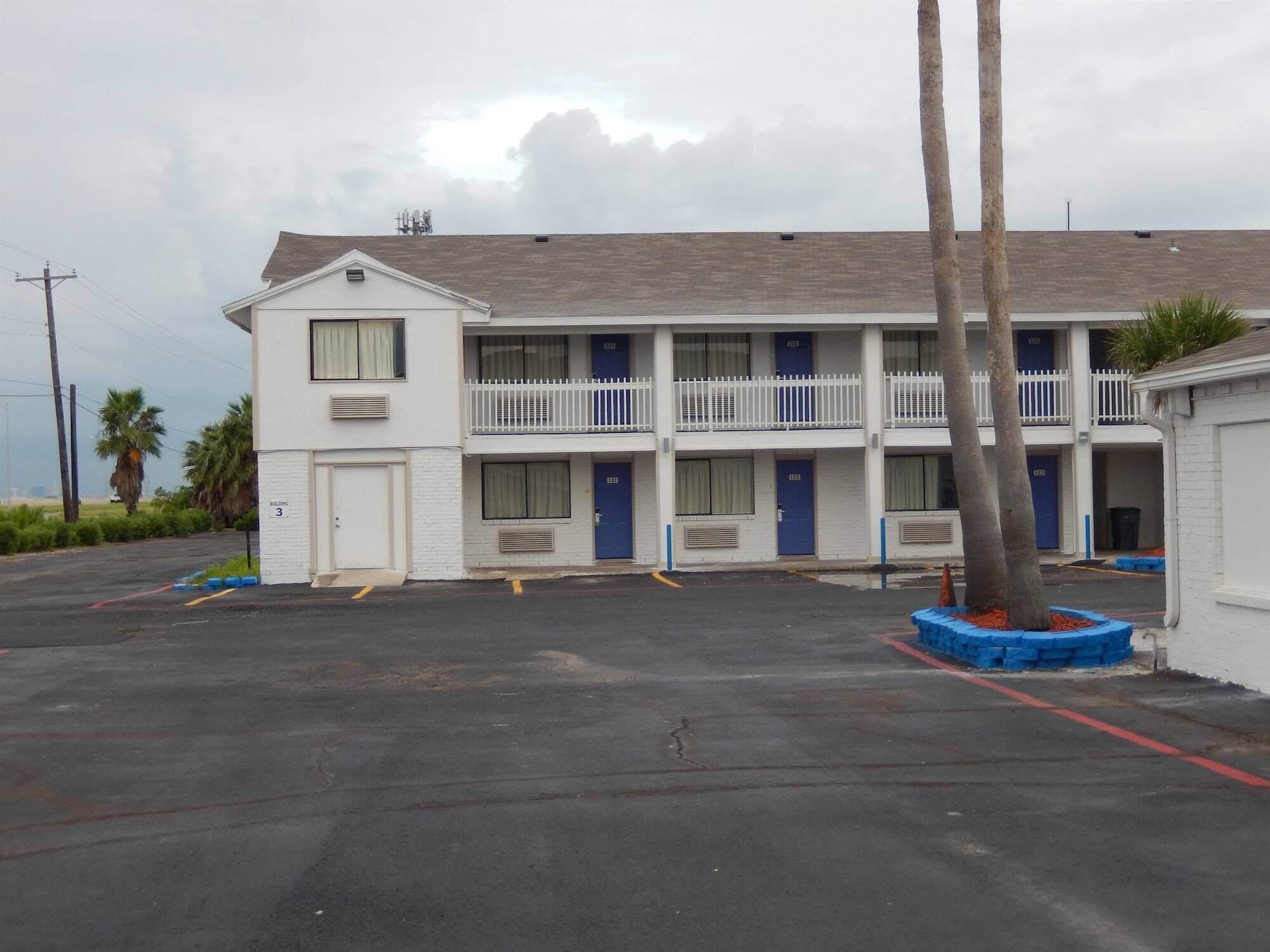 A motel with a two-story structure, multiple rooms with blue doors, and a parking lot.