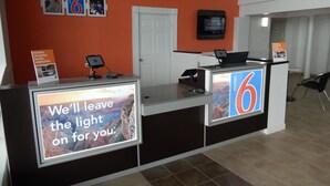 A hotel reception desk with a large screen displaying a message, a digital kiosk, and a sign indicating the hotel name '6'. - Motel 6 Portland, TX (Portland)