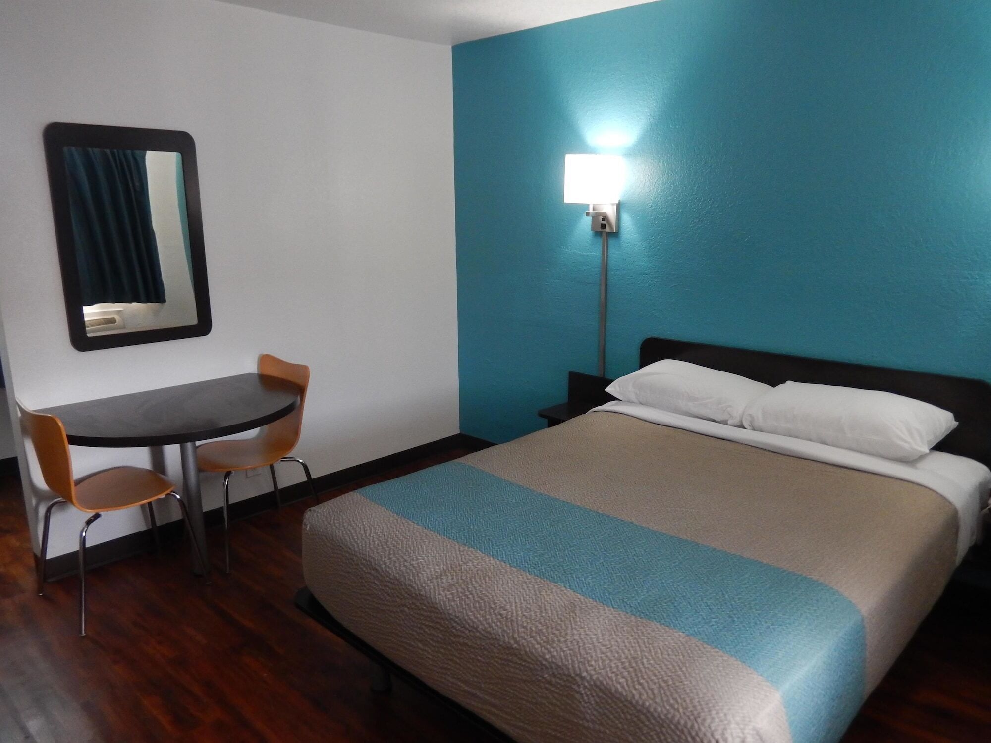 Une chambre d’hôtel comprenant un lit, un bureau, une chaise et une table de chevet avec une lampe.
