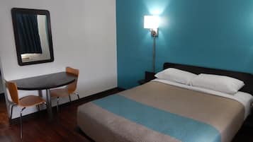Une chambre d’hôtel comprenant un lit, un bureau, une chaise et une table de chevet avec une lampe.