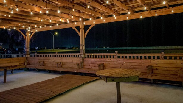 An outdoor wooden pavilion with benches and tables, featuring a wooden ceiling with exposed beams and string lights. - Motel 6 Portland, TX (Portland)