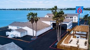 A hotel with a parking lot, a beach view, and a sign indicating the number 6. - Motel 6 Portland, TX (Portland)