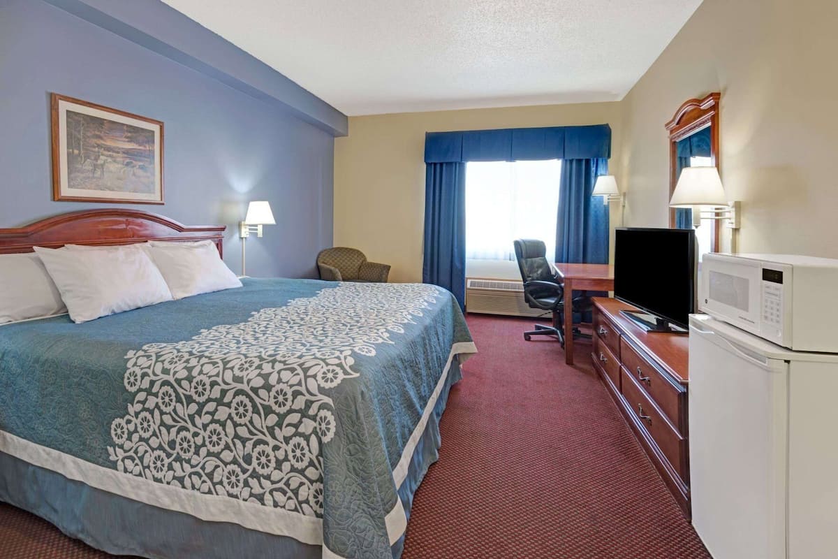 A hotel room with a bed, desk, chair, television, and microwave.