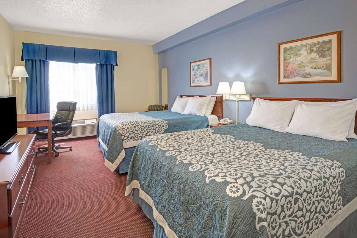 A hotel room with two beds, a desk, a chair, and a television.