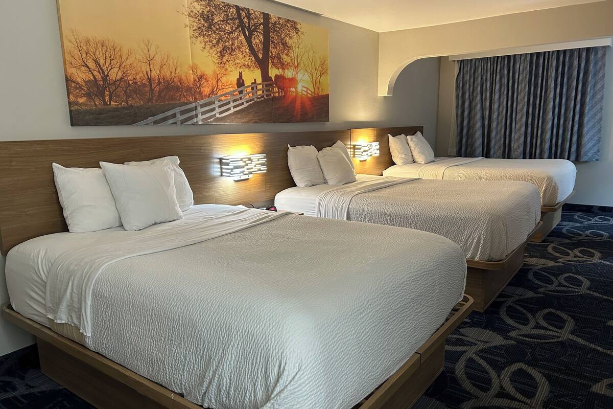 A hotel room with two beds, each with white bedding and headboards. There is a large painting of a sunset scene on the wall above the beds.