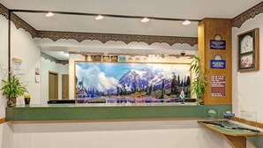 Mostrador de recepción con un mural panorámico de un paisaje montañoso, un reloj y premios por calidad.