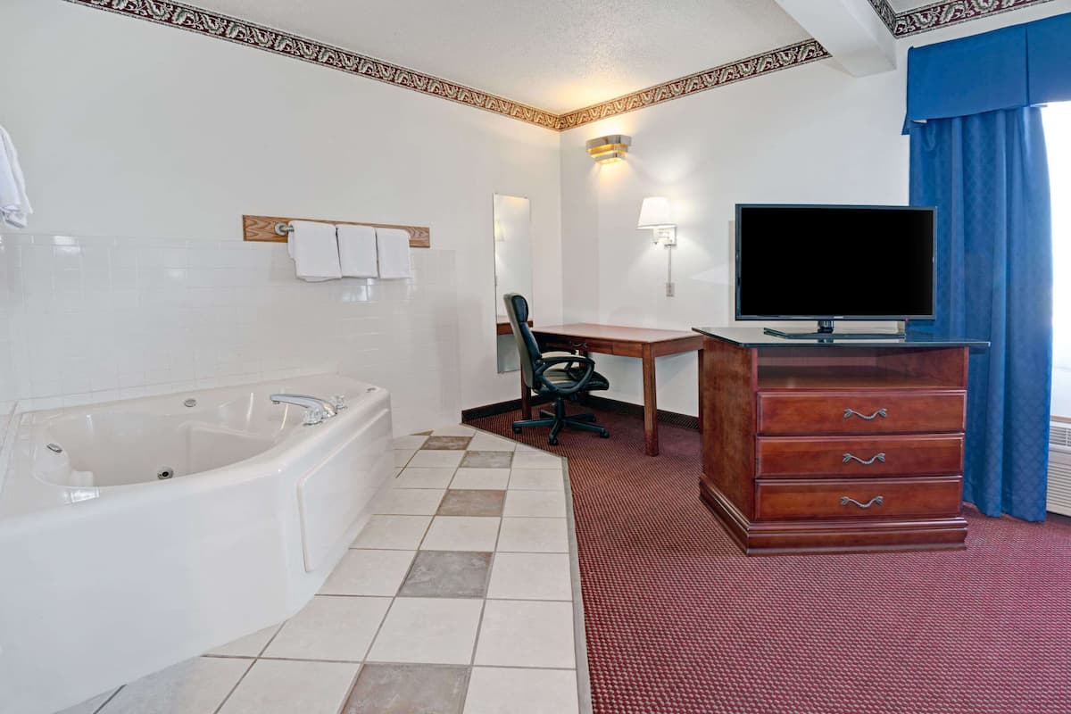 A hotel bathroom with a bathtub, a wooden desk, a television, and a dresser.