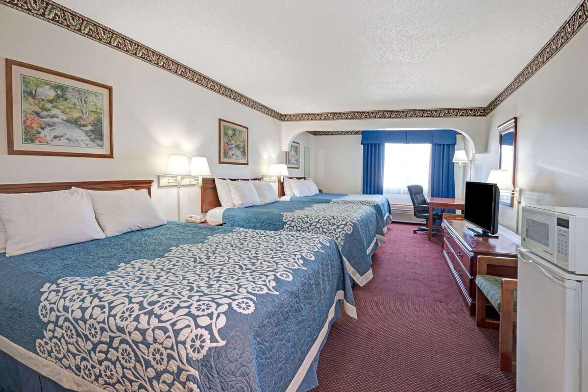 A hotel room with two beds, a desk with a TV, a microwave, and a chair.