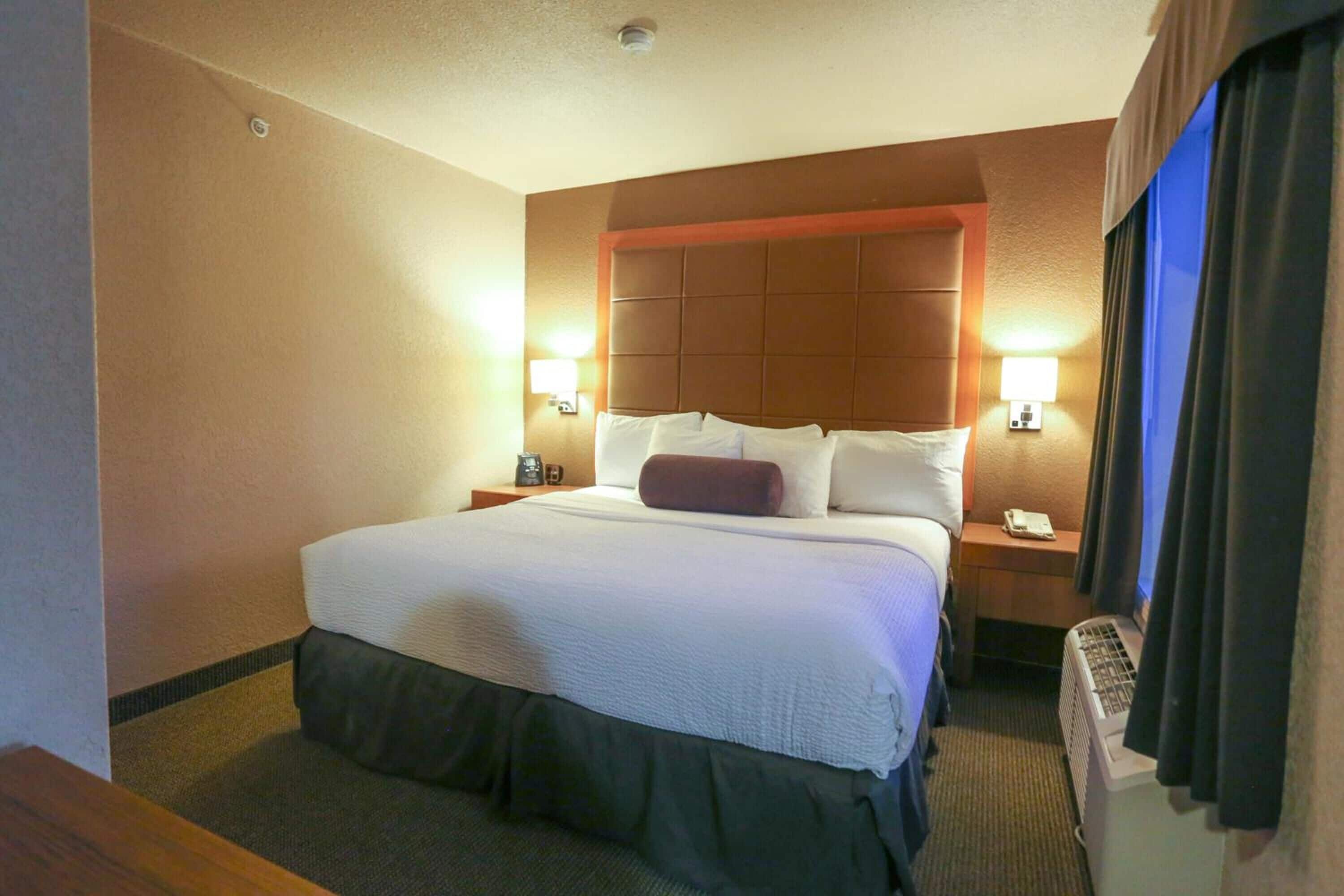 A hotel room with a large bed, two bedside tables, a wall-mounted heater, and two wall-mounted lamps.