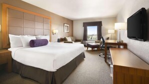 Une chambre d’hôtel avec un grand lit, un bureau, une chaise, une télévision et une fenêtre donnant sur un beau paysage.