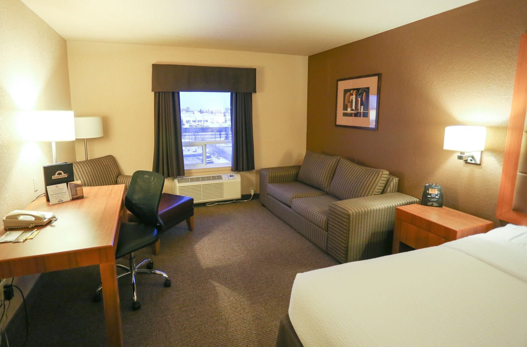 A hotel room with a desk, chair, couch, and bed.