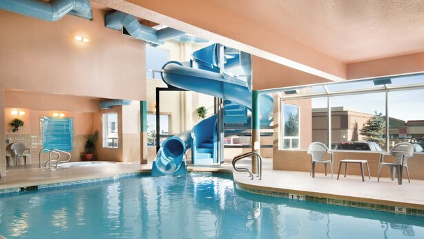 Une piscine intérieure avec un toboggan à eau bleu, des chaises longues et une vue sur l’extérieur.