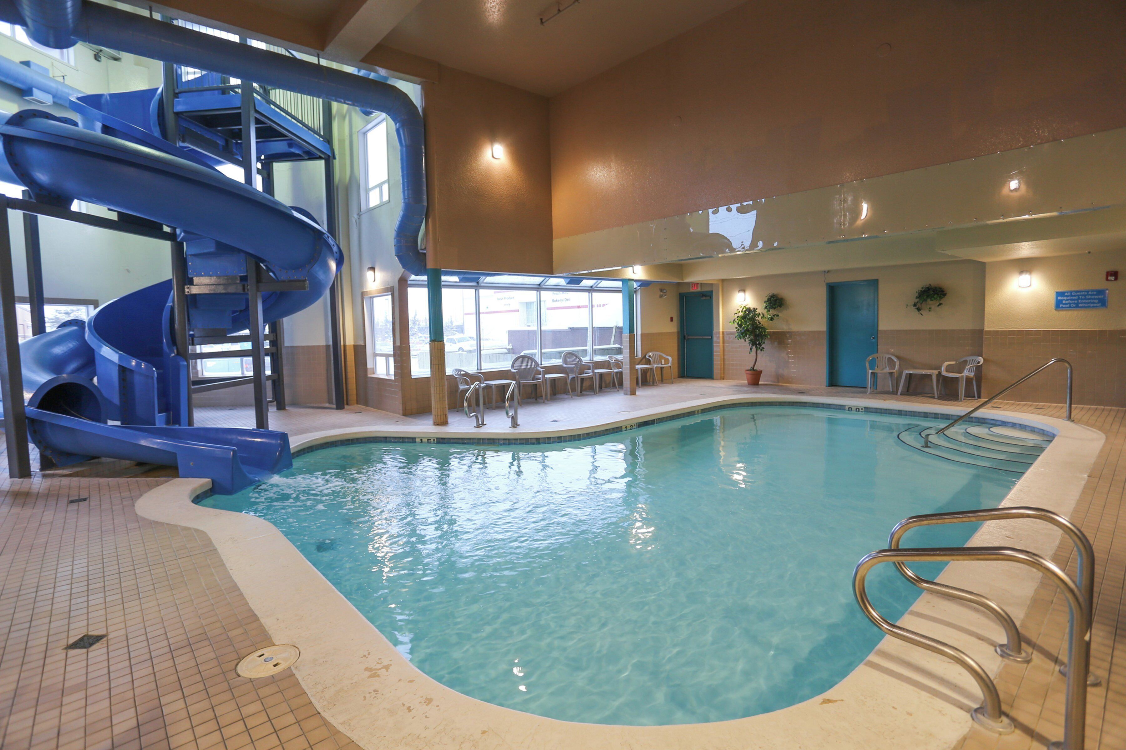 An indoor swimming pool with a blue slide, poolside chairs, and a sunroof.
