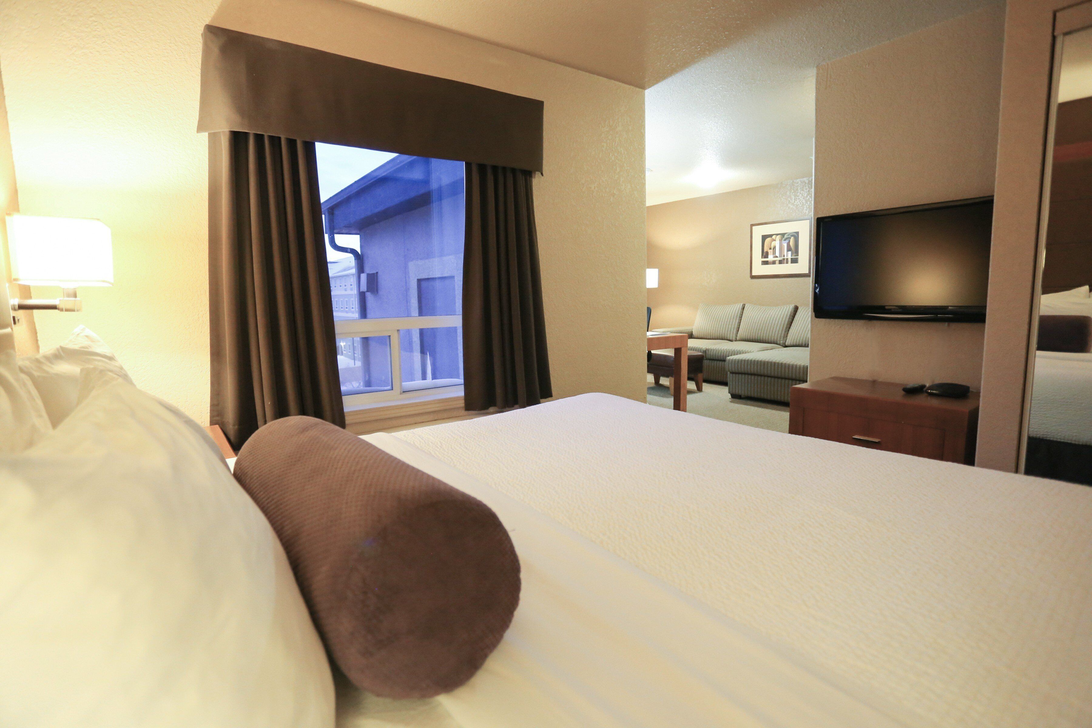 A hotel room with a bed, a television, a window with curtains, a sofa, and a desk.