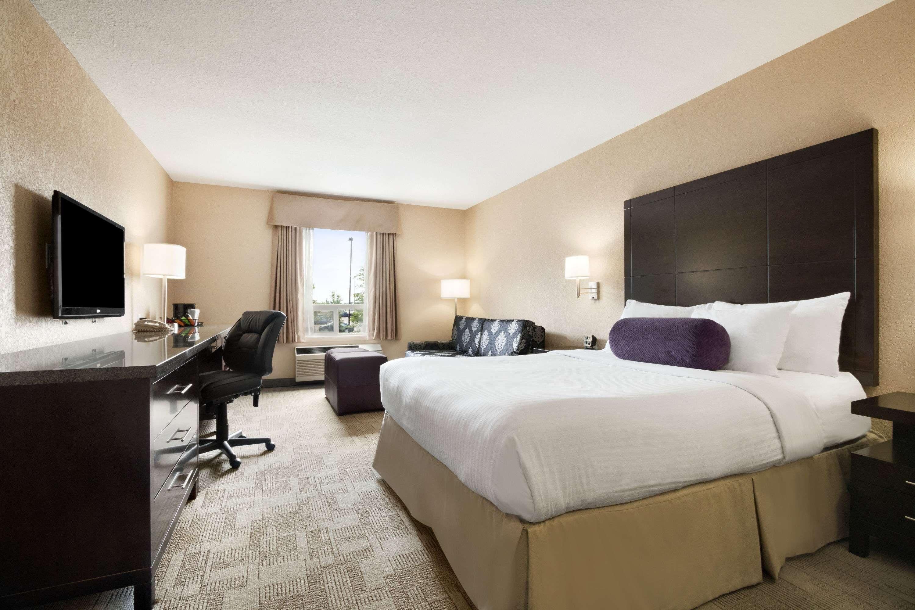 A hotel room with a large bed, a desk, a chair, a TV, and a window with curtains.
