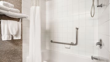 A bathroom with a bathtub, a shower, a grab bar, and a towel rack with folded towels.