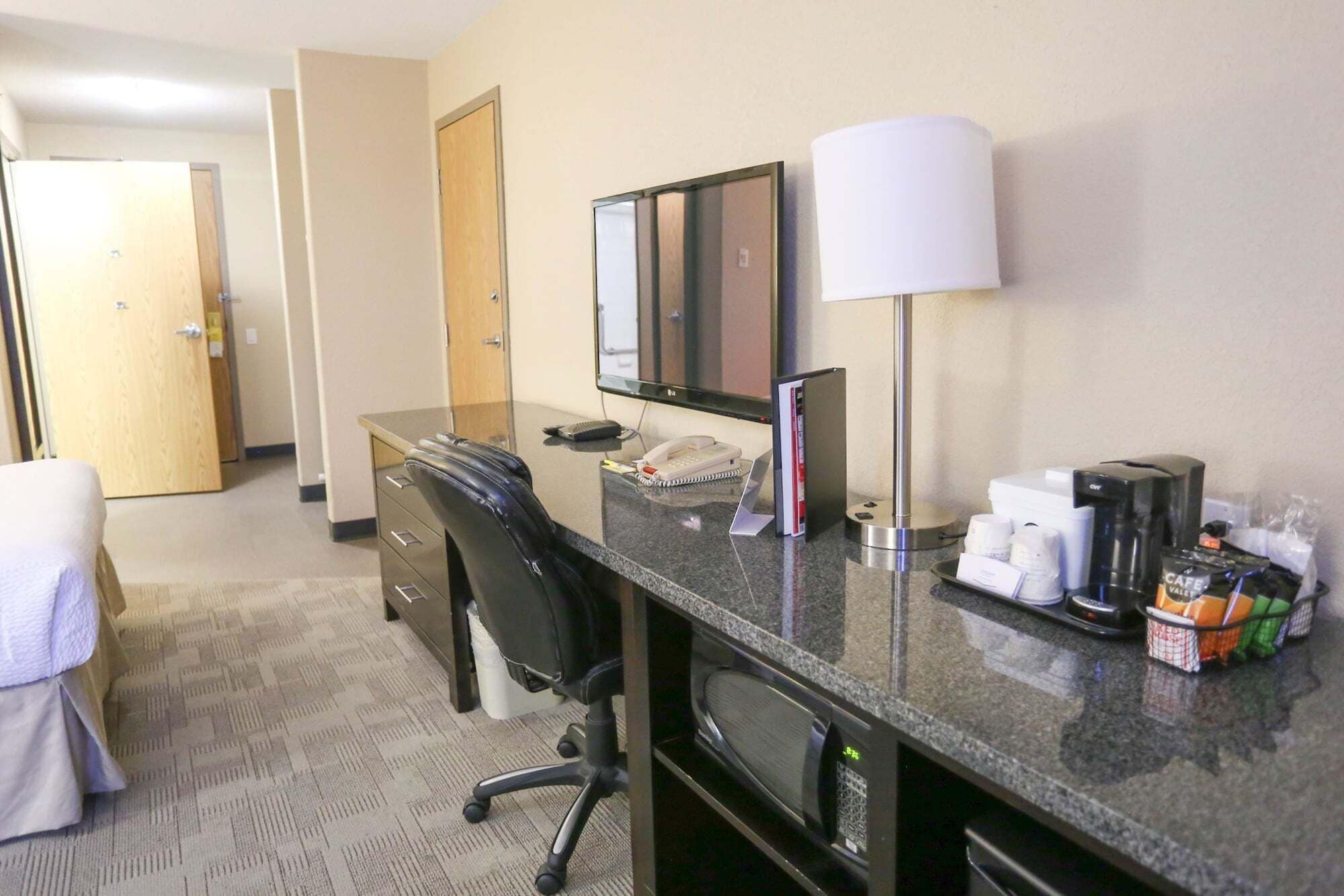 Habitación de hotel con escritorio, silla, lámpara, teléfono, cafetera y artículos de aseo.