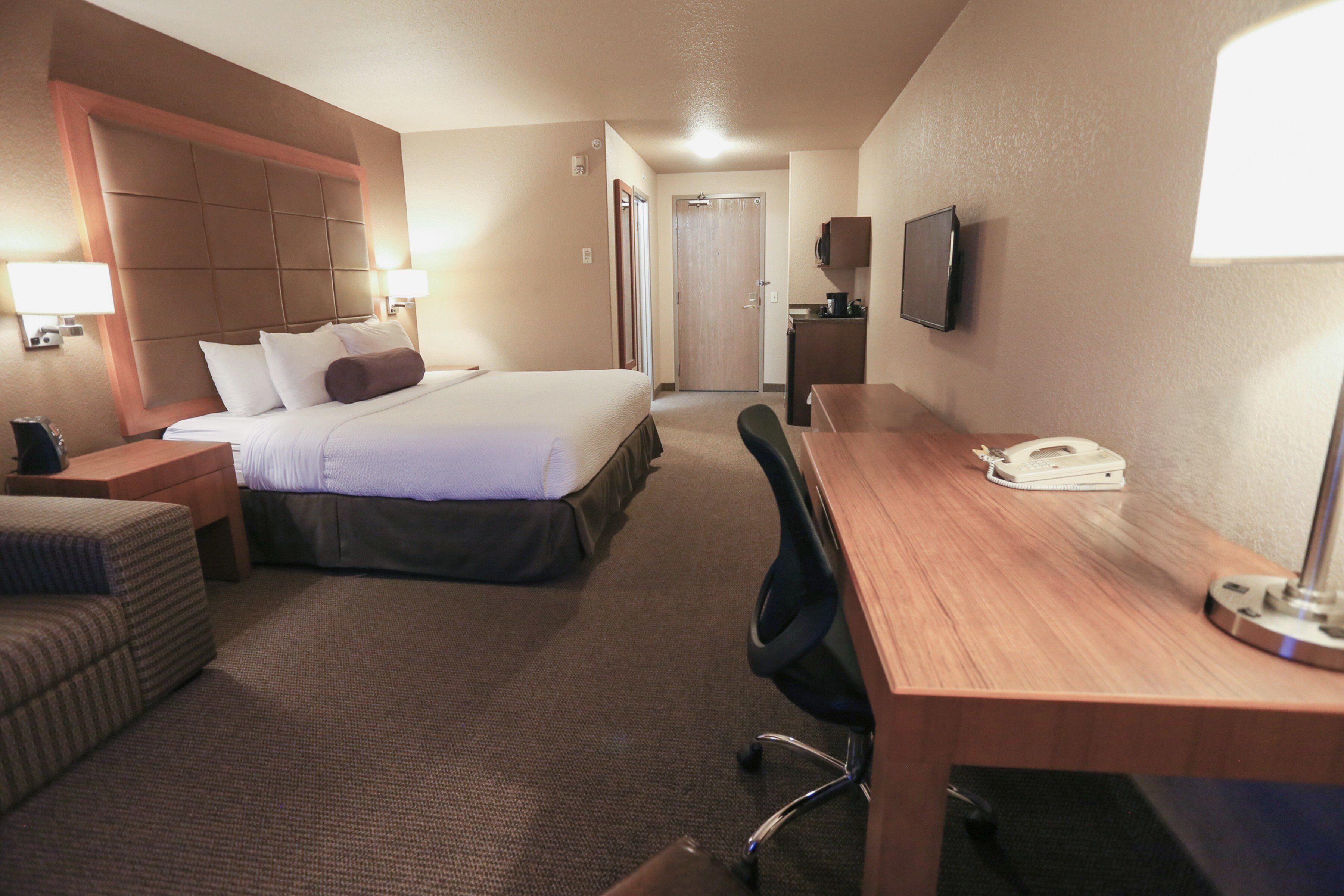 A hotel room with a bed, a desk, a chair, a TV, and a lamp.