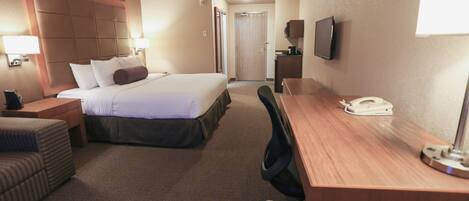 A hotel room with a bed, a desk, a chair, a TV, and a lamp.