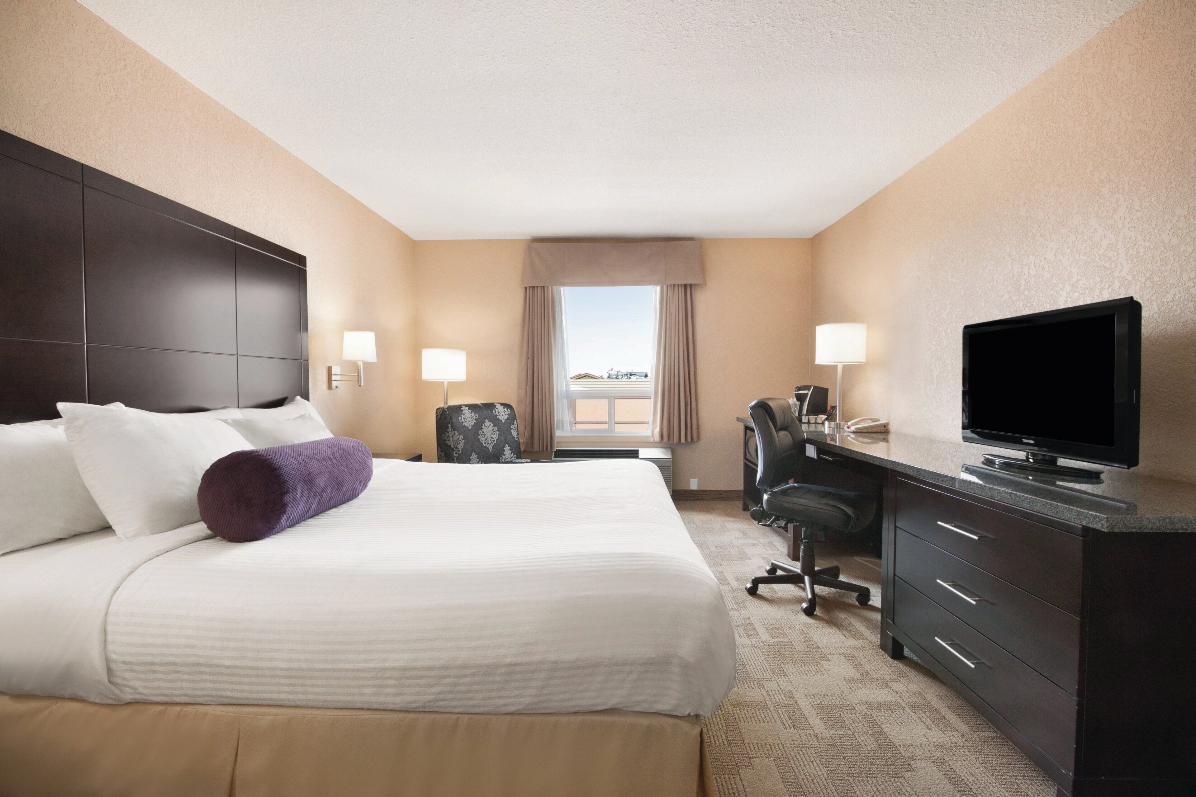 A hotel room with a bed, desk, television, and a view of the cityscape.