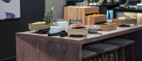 A breakfast bar with wooden stools, a fruit display, and a coffee machine in the background.