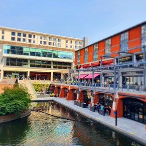 A riverside walkway with a modern building in the background, a bridge, and a restaurant with outdoor seating. - AC Hotel by Marriott Birmingham (Birmingham)