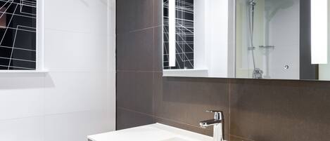 Un baño moderno con un espejo grande, un lavabo blanco y una zona de ducha.