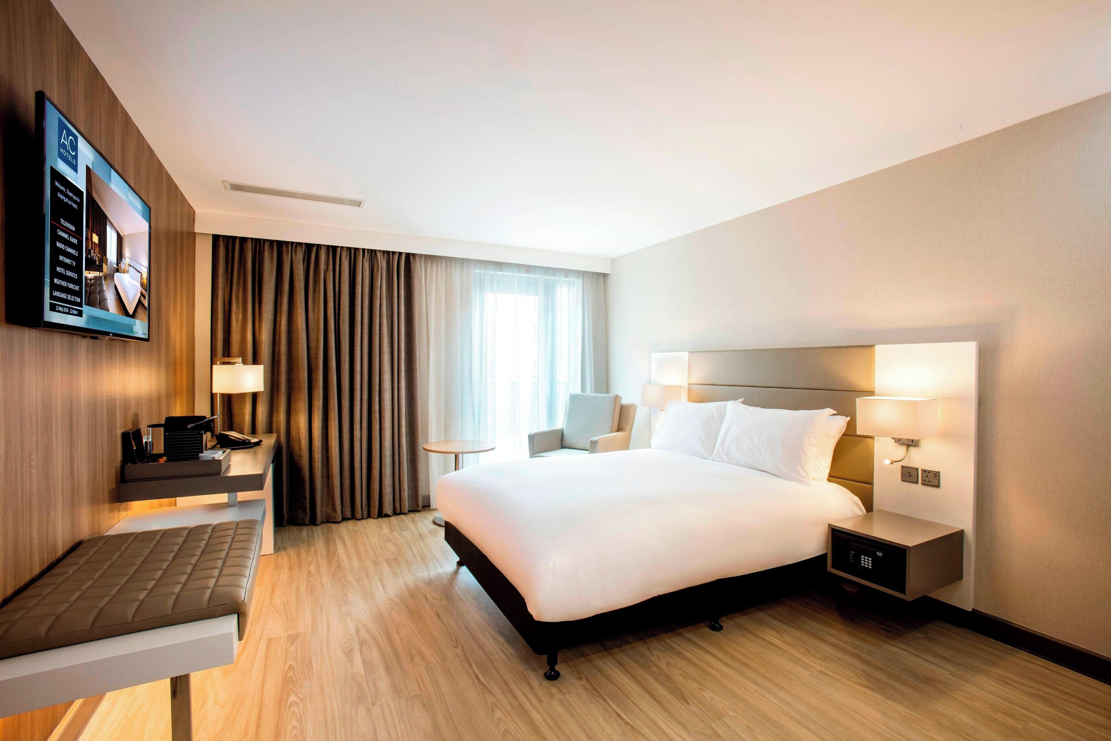 A modern hotel room with a large bed, bedside tables, a desk, and a television displaying room amenities.