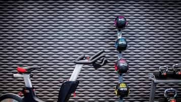 Un vélo d'appartement doté d'un écran numérique et d'une pile de poids fixée au mur, avec différents poids disponibles.