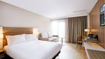 A modern hotel room with a large bed, a sofa, a small table, and a desk with a chair.
