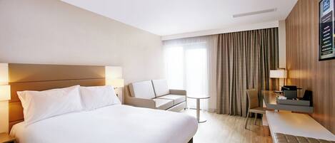Una habitación de hotel moderna con una cama grande, un sofá, una mesita y un escritorio con una silla.