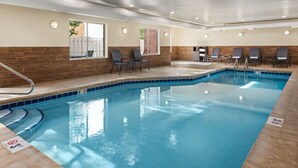 Une piscine intérieure avec un bord carrelé, un escalier d’accès et plusieurs chaises longues disposées autour de la piscine.