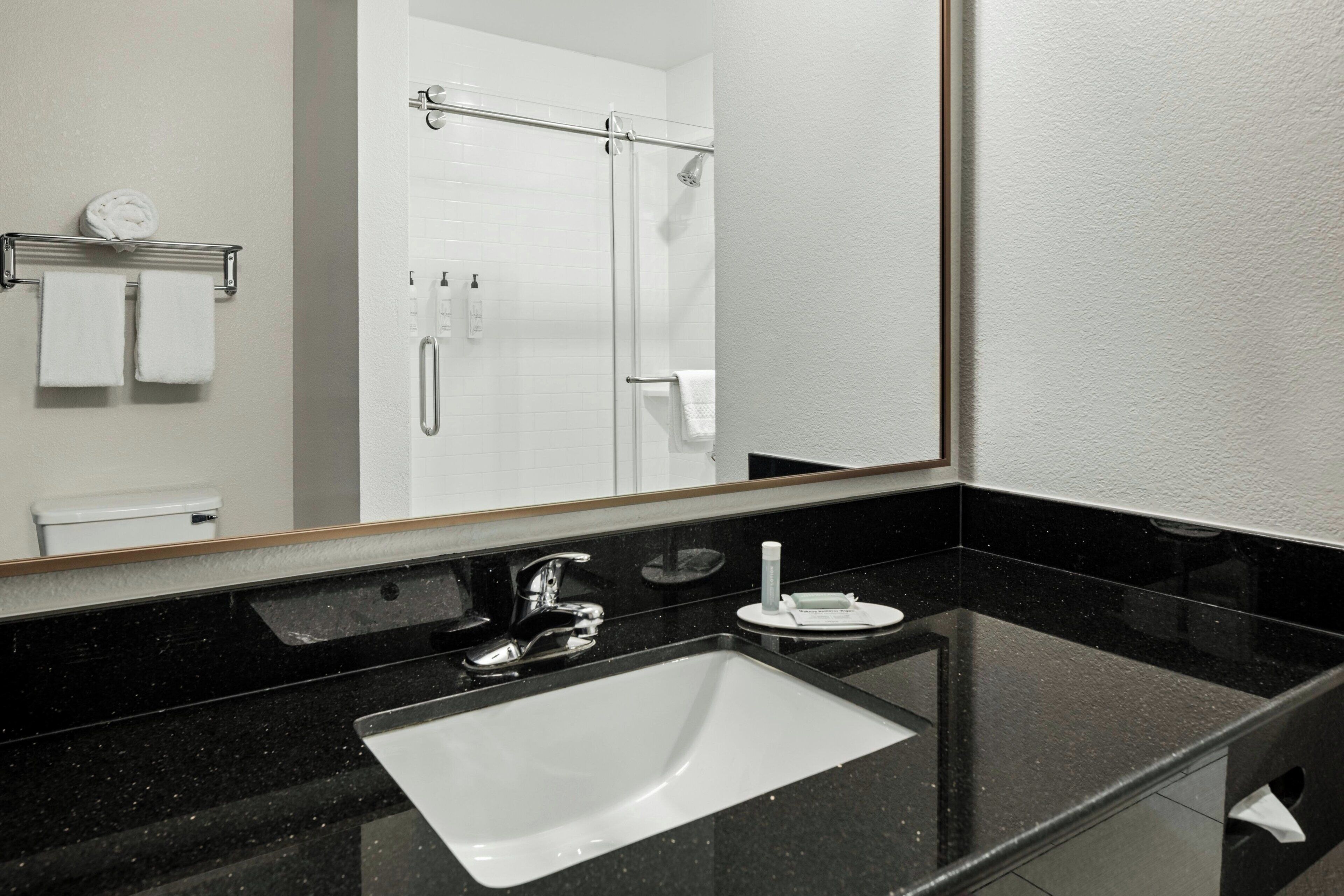 A modern bathroom with a black countertop, a white sink, a mirror, and a shower area.
