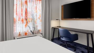 A hotel room with a bed, a desk, a chair, a flat-screen TV, and a window with curtains.