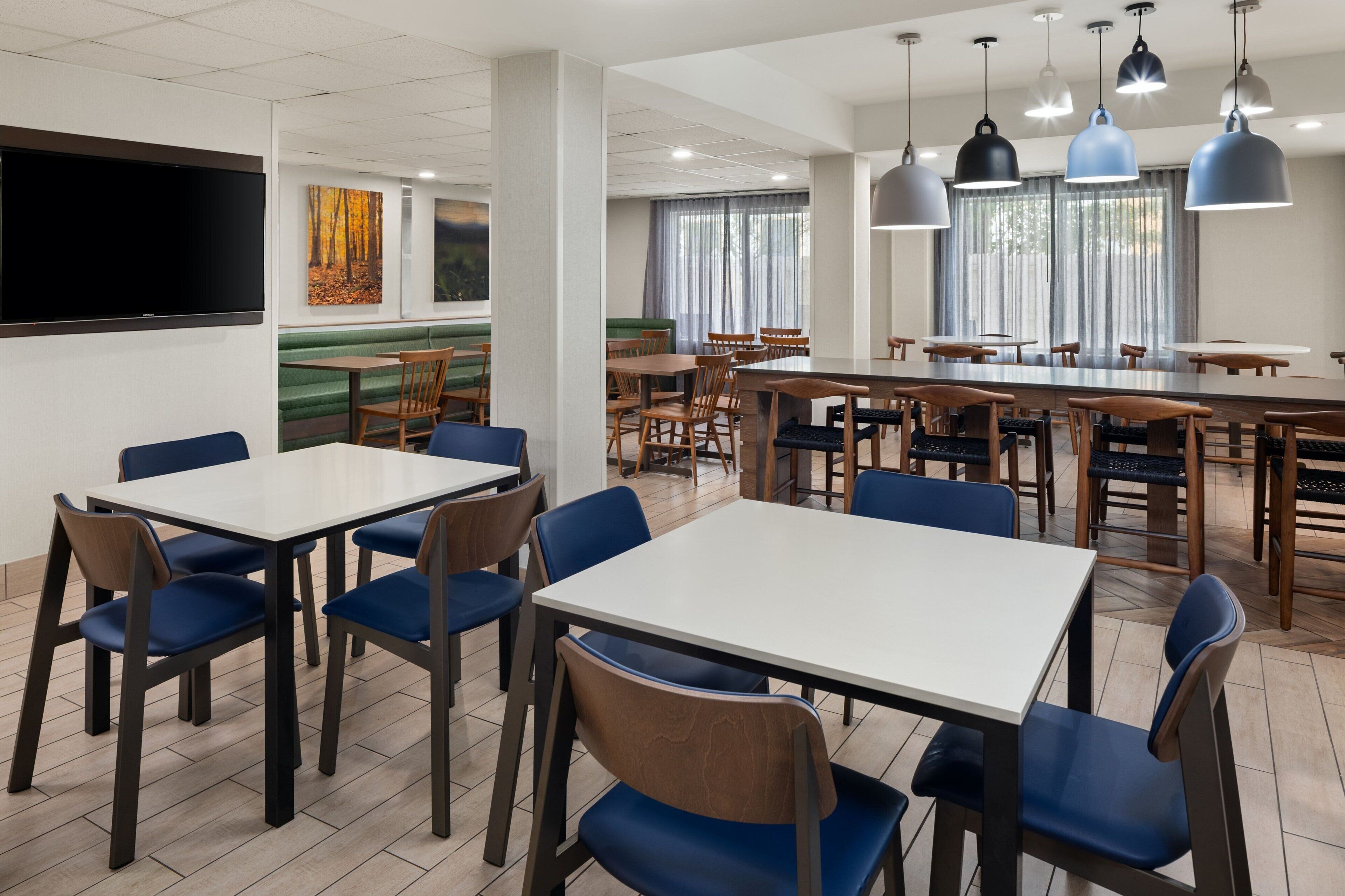 A modern dining area with multiple tables and chairs, a flat-screen TV mounted on the wall, and artwork on the walls.