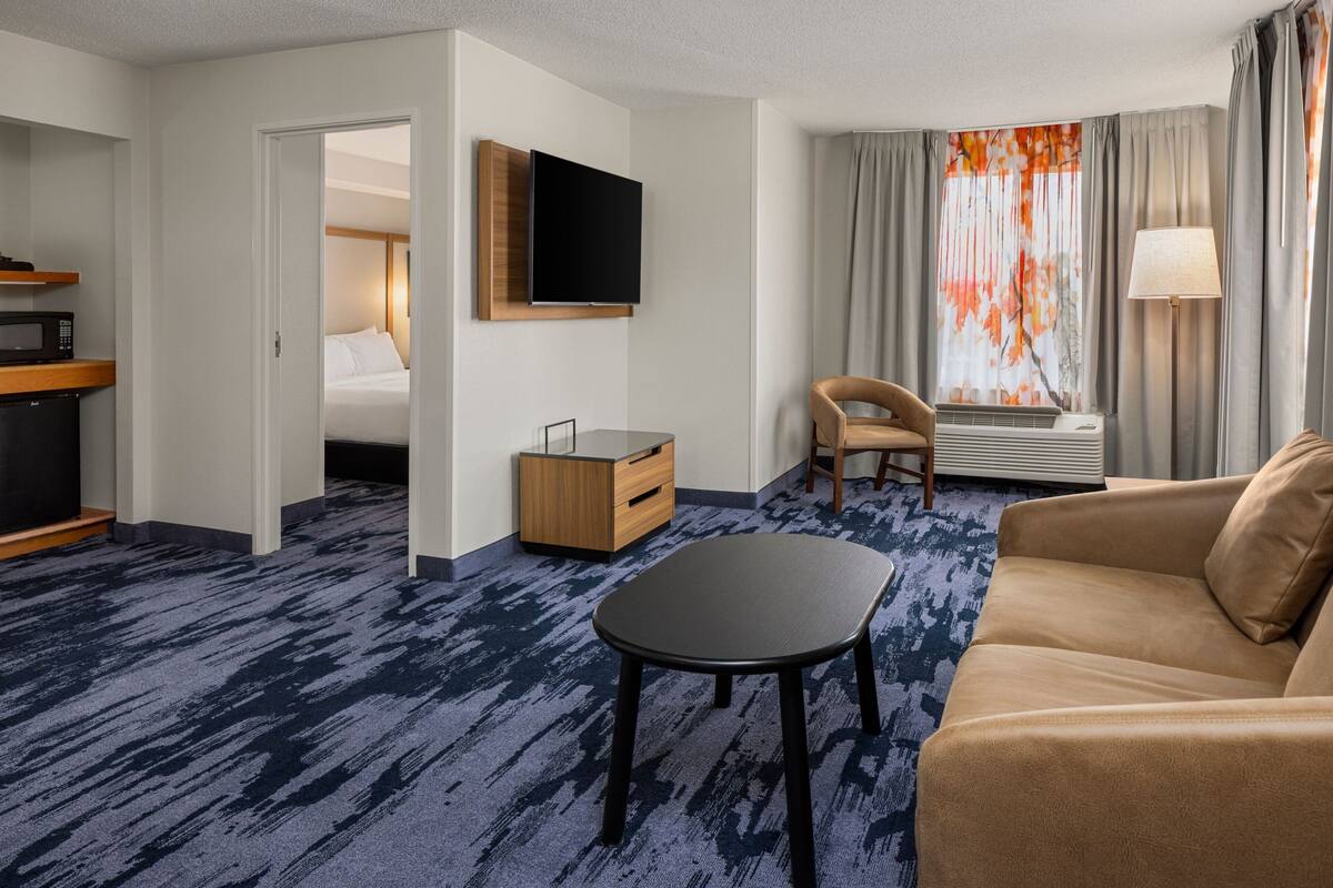 A hotel room with a bed, a TV, a sofa, a coffee table, and a desk with a lamp.
