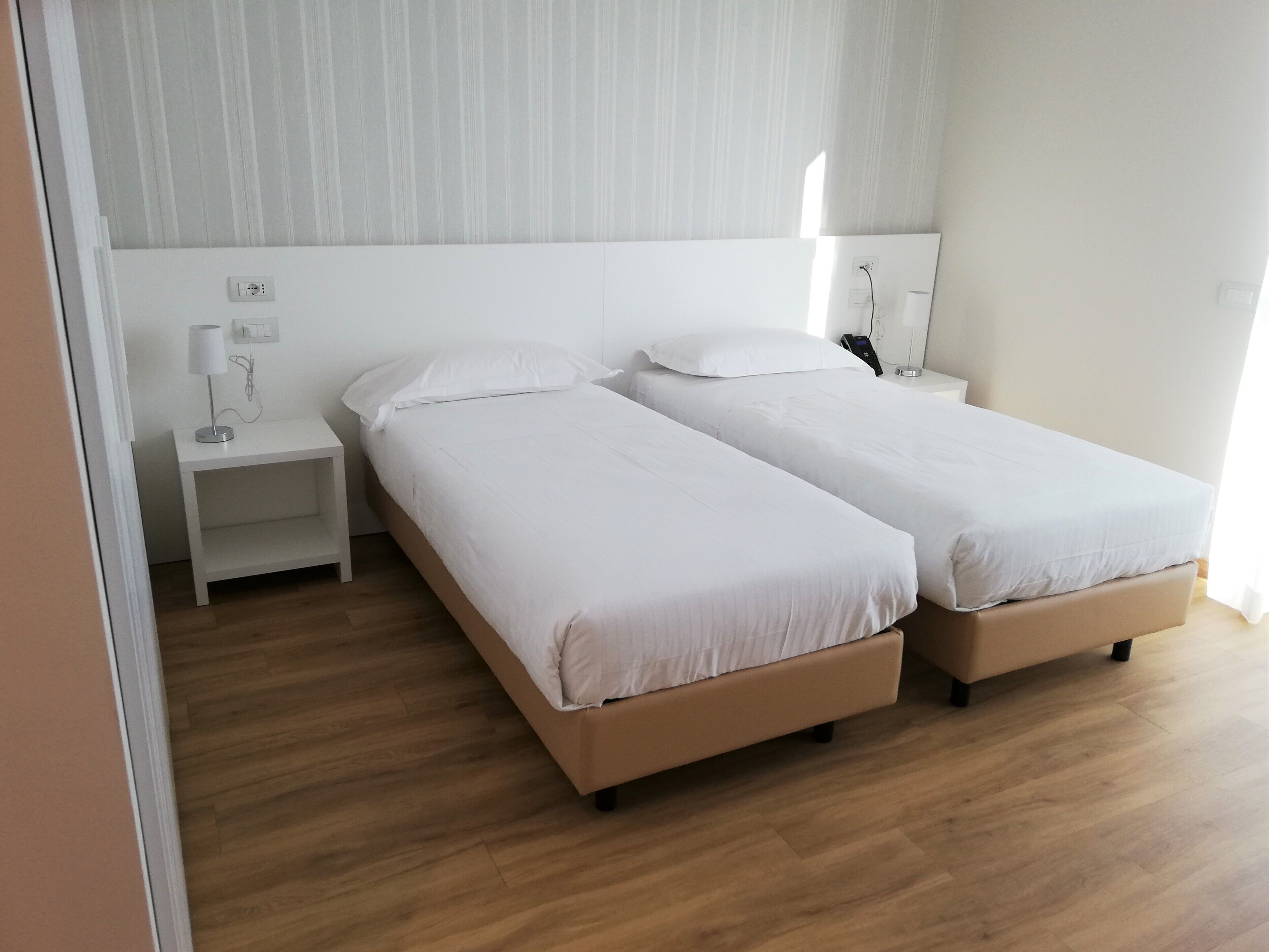 A hotel room with two single beds, a bedside table with a lamp, and a nightstand with a phone.
