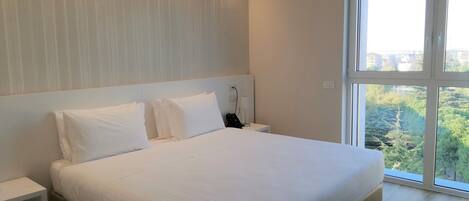 A modern bedroom with a large bed, a nightstand, and a window with a city view.