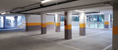 Un garaje para estacionar con pilares de hormigón, iluminación fluorescente y un extintor.