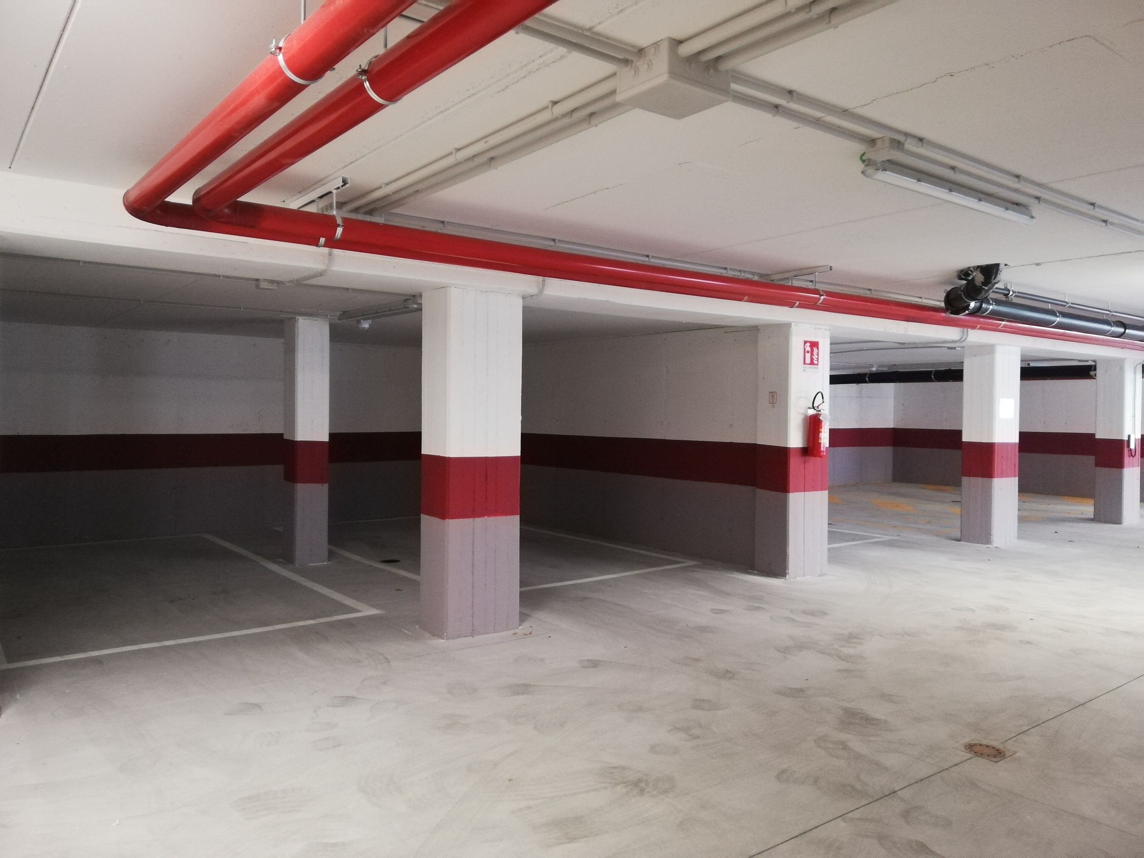 An empty parking garage with concrete pillars and red and white painted stripes.