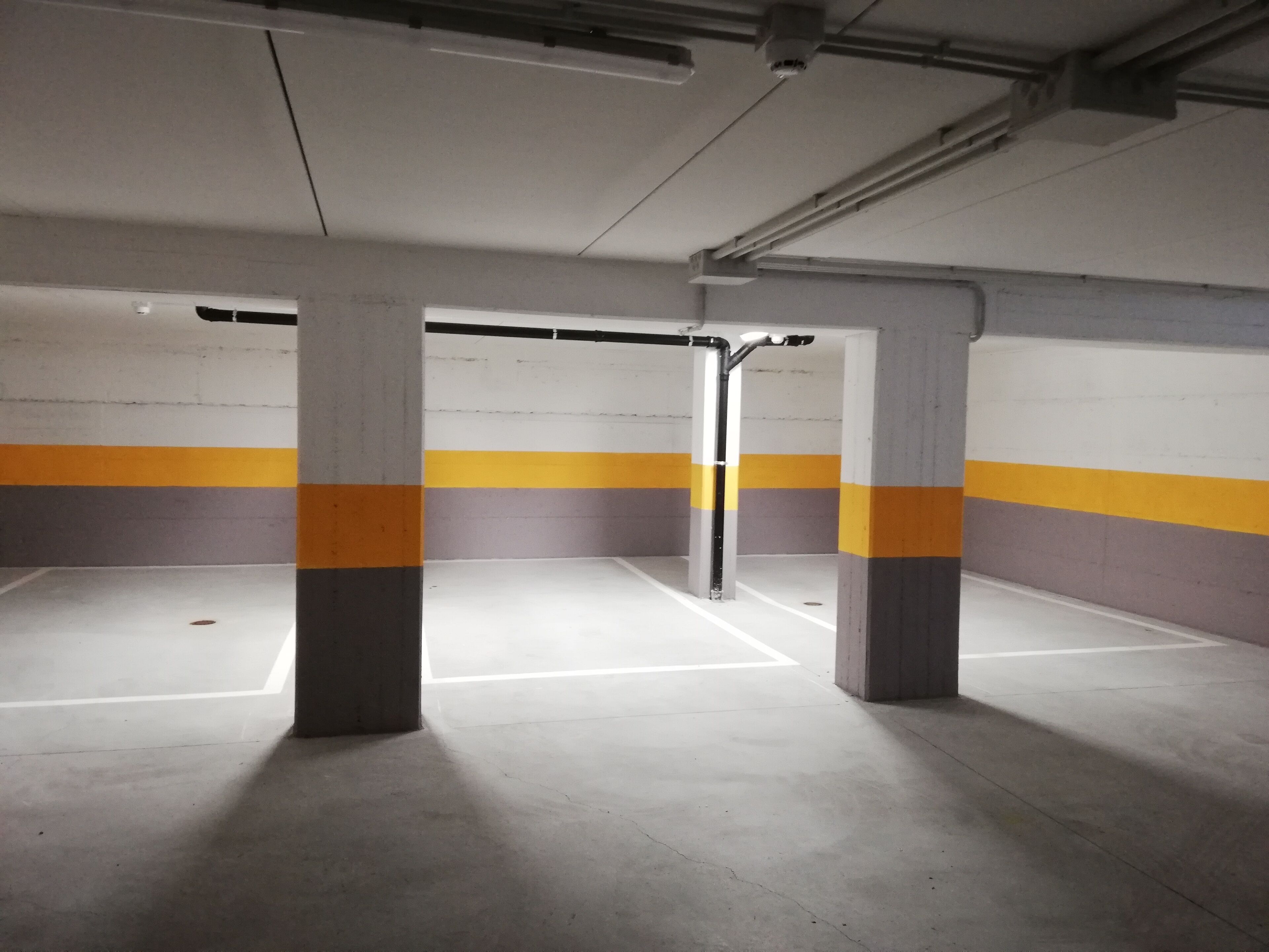 An empty parking garage with concrete pillars and yellow and gray painted walls.