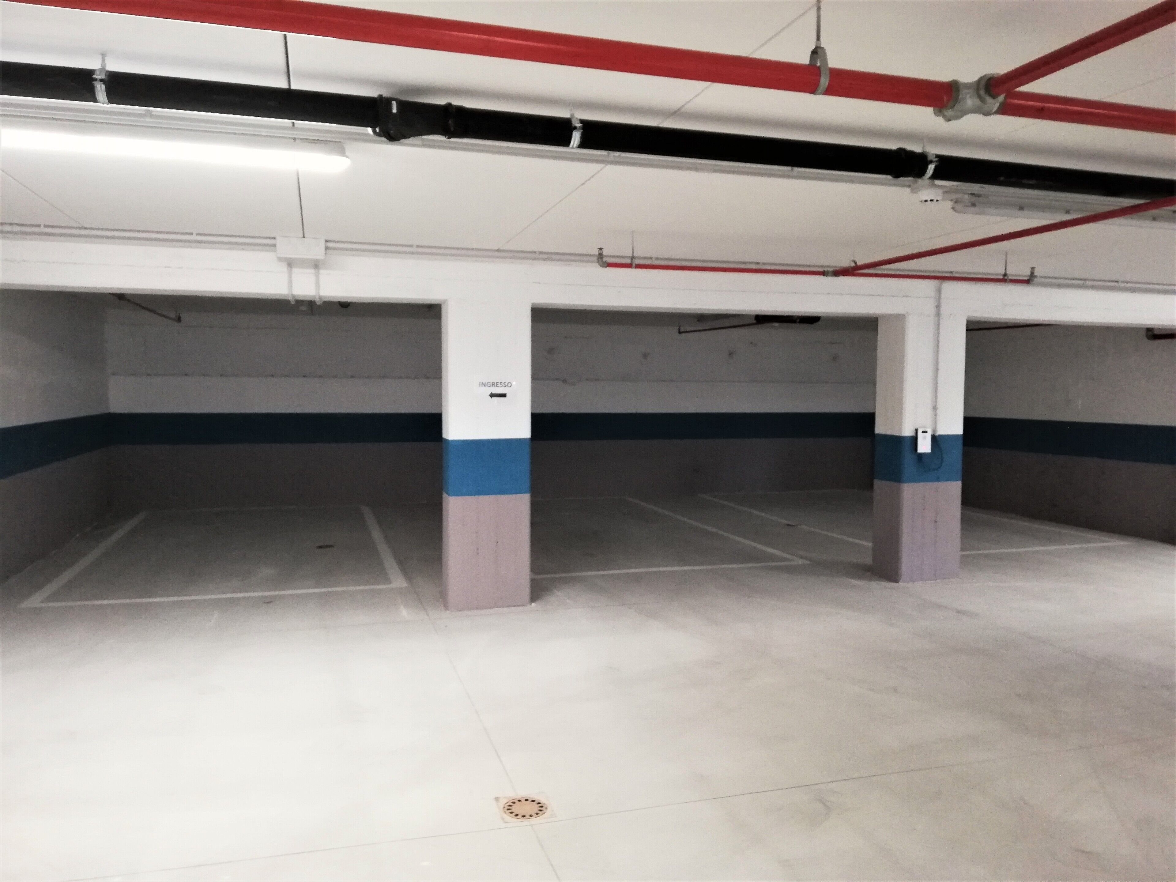 Un estacionamiento vacío con pilares de hormigón, franjas blancas y azules, y tuberías rojas.