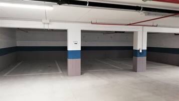 Un estacionamiento vacío con pilares de hormigón, franjas blancas y azules, y tuberías rojas.