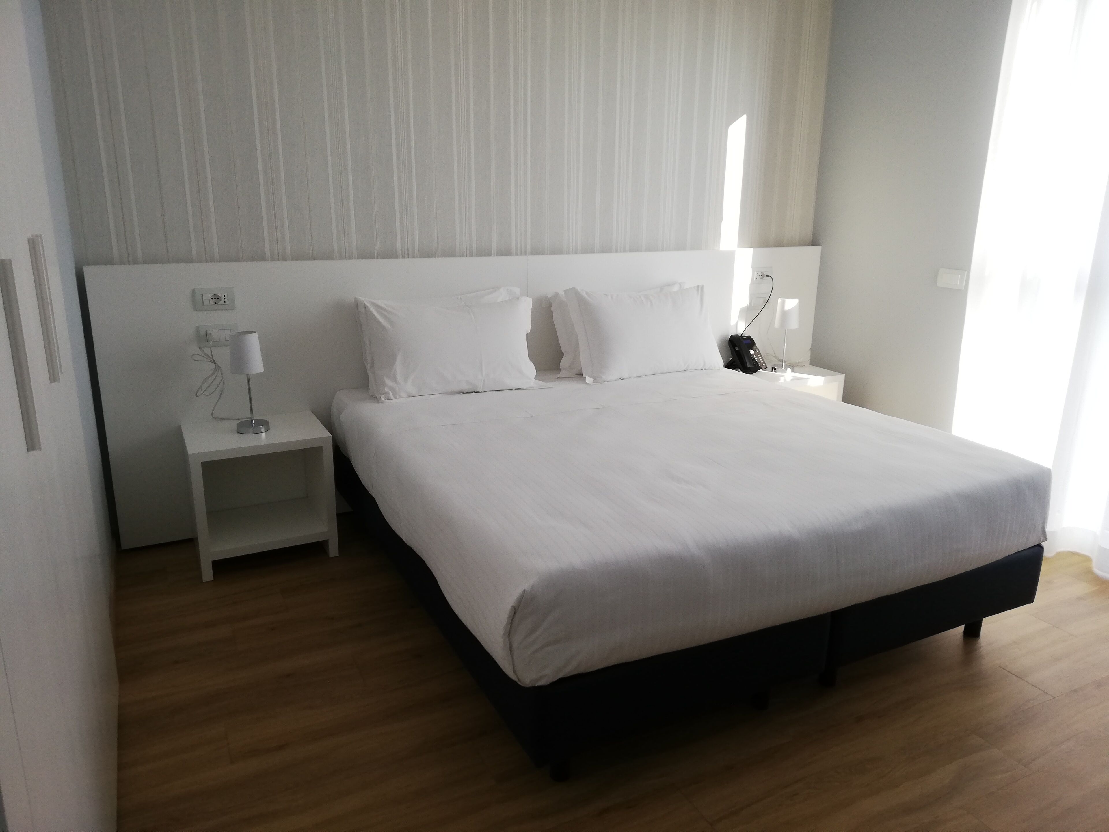 A neatly arranged hotel room with a large bed, a bedside table, a lamp, and a phone.