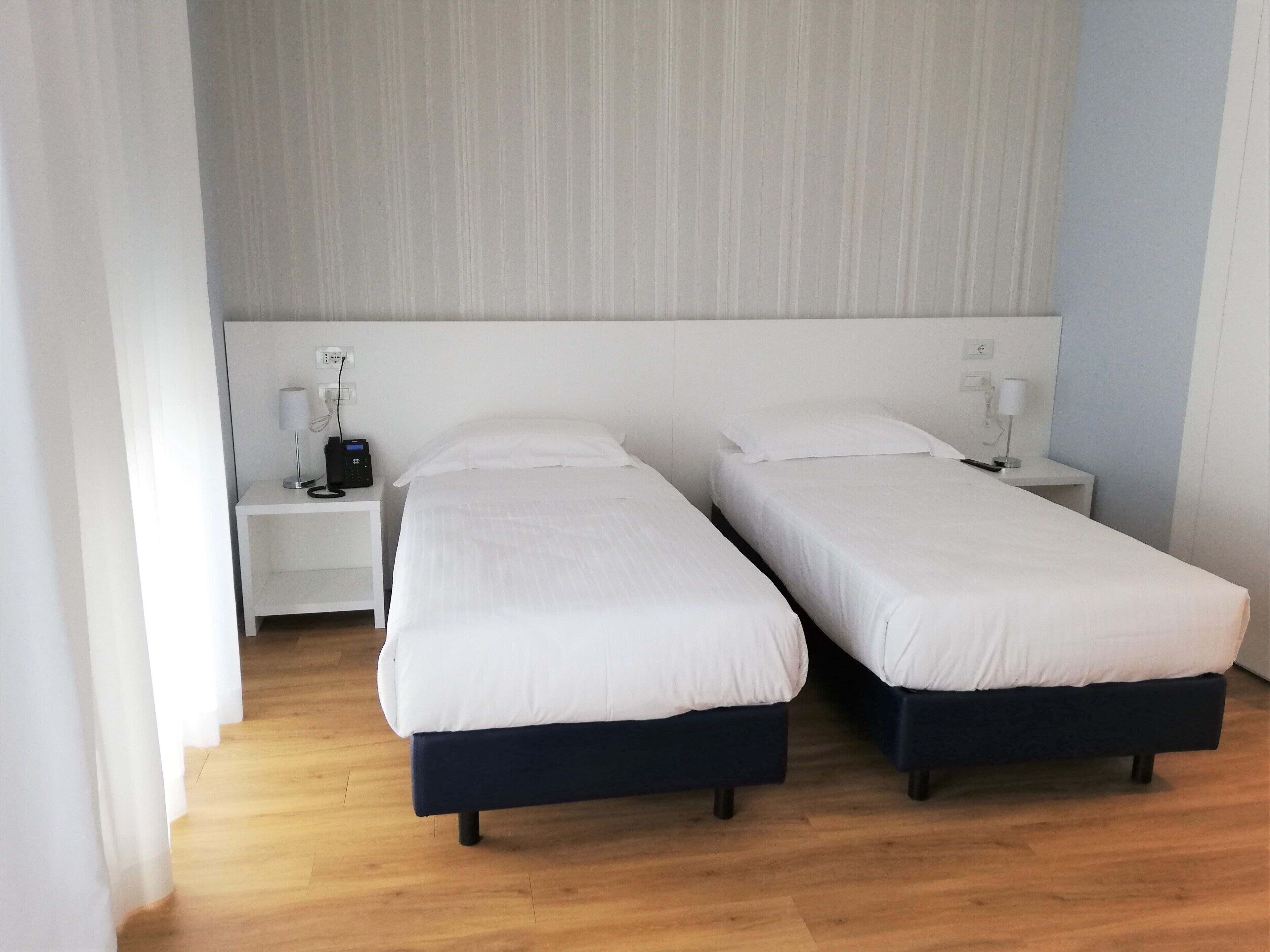 Une chambre d’hôtel avec deux lits simples, une table de chevet avec une lampe et une prise électrique au mur.