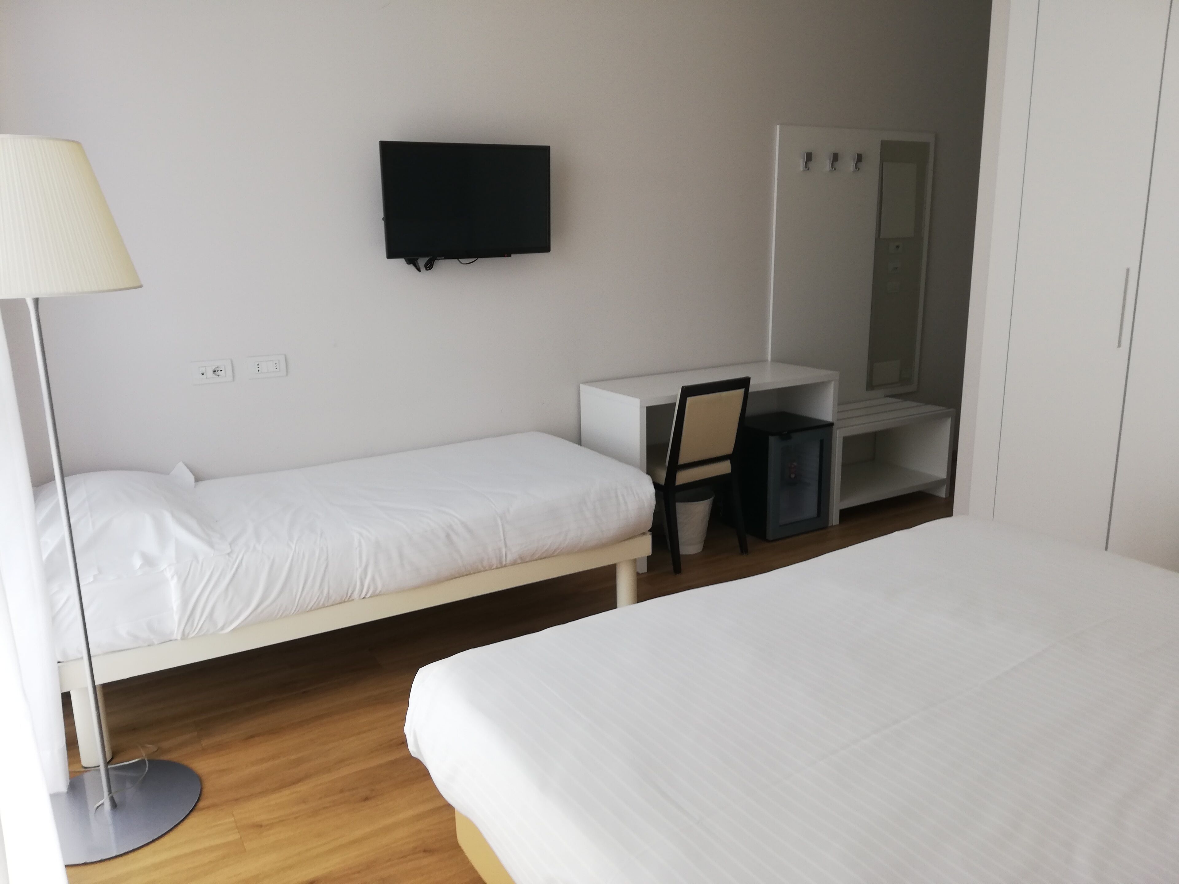 A hotel room with two single beds, a desk with a chair, a television, and a wardrobe.
