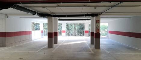 Un estacionamiento vacío con pilares de hormigón, paredes pintadas de rojo y blanco y un techo de metal.