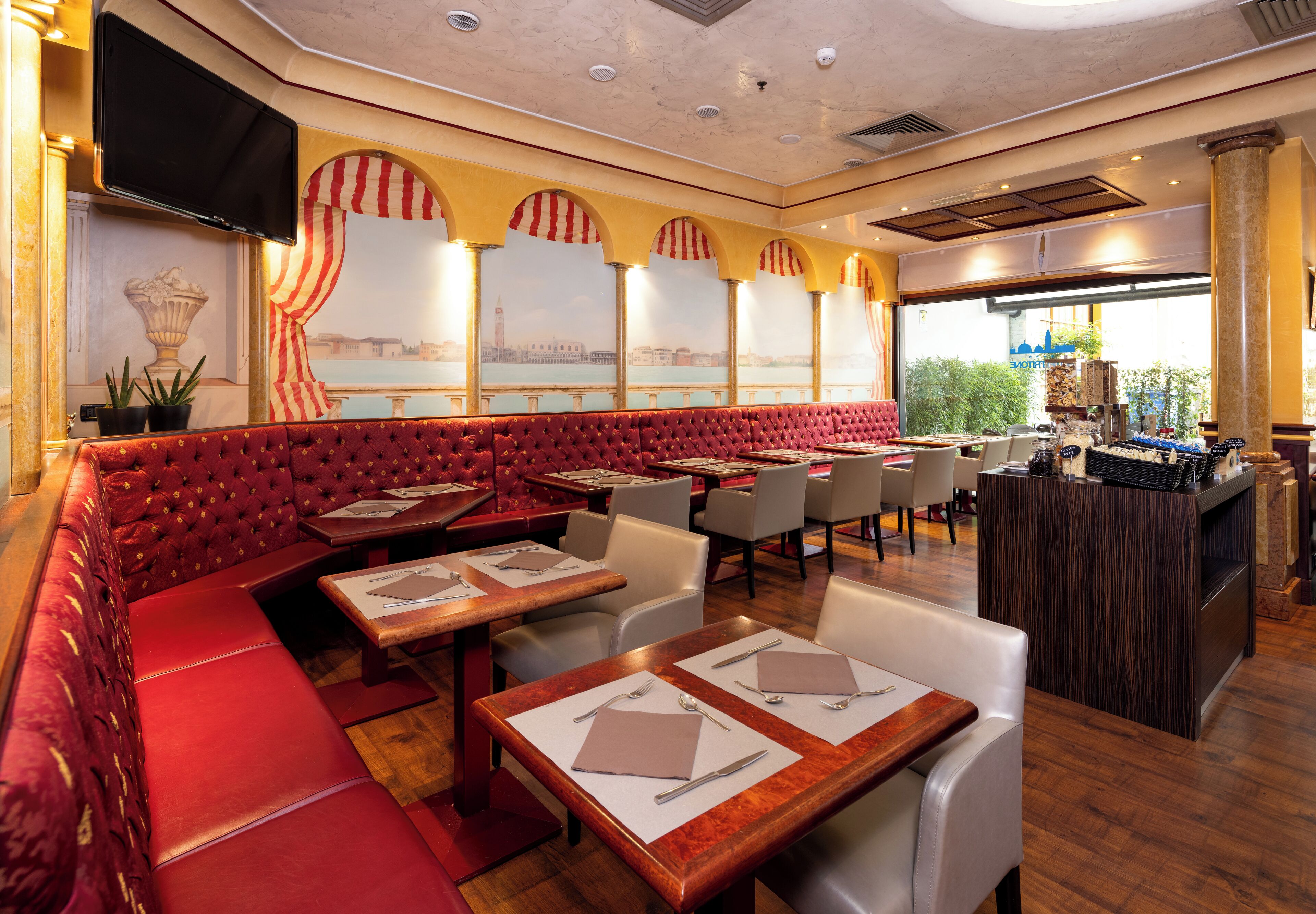 A restaurant with red upholstered booths, white tables, and a bar area.