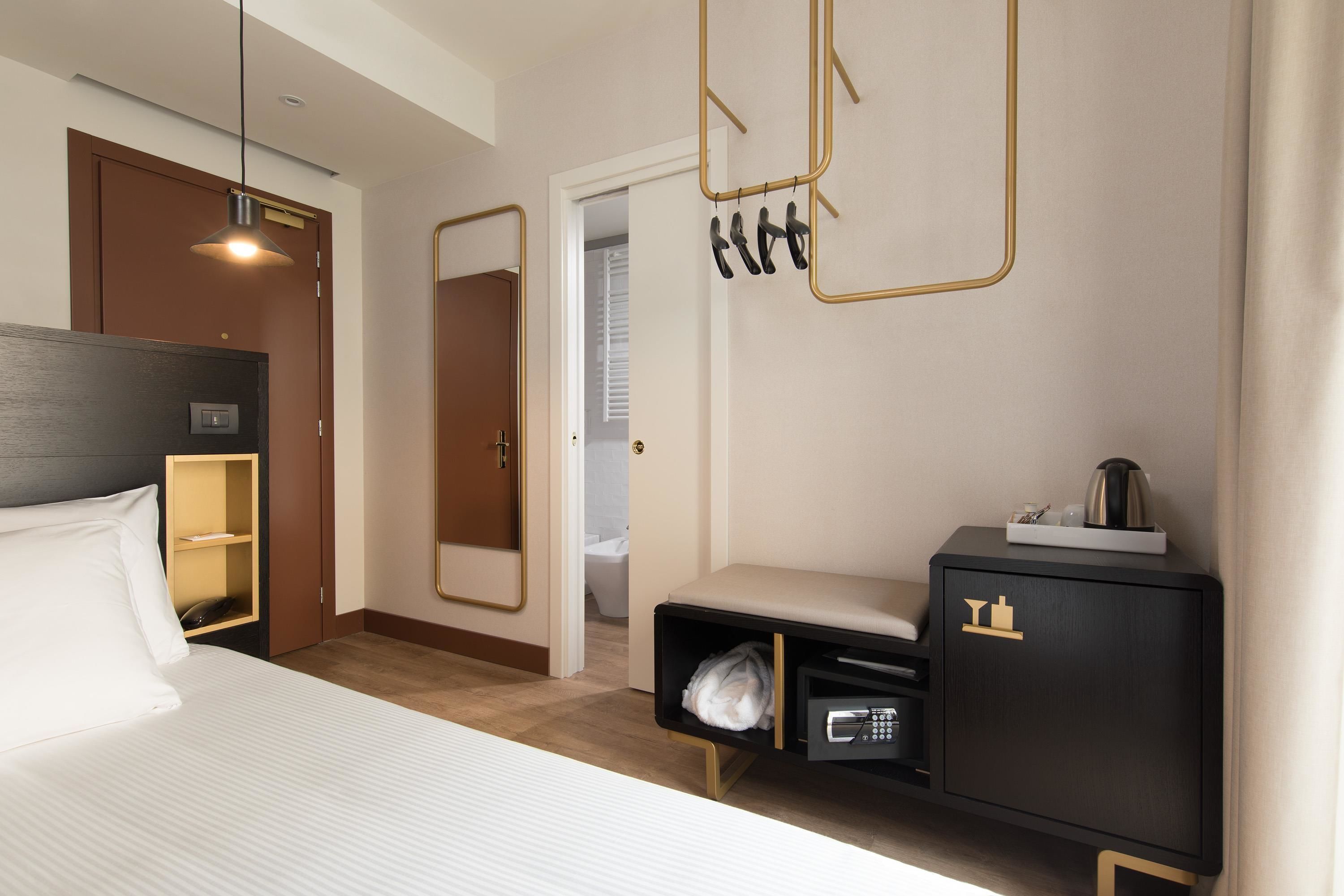 A hotel room with a bed, a wardrobe, a bedside table, a mirror, and a hanging light fixture.