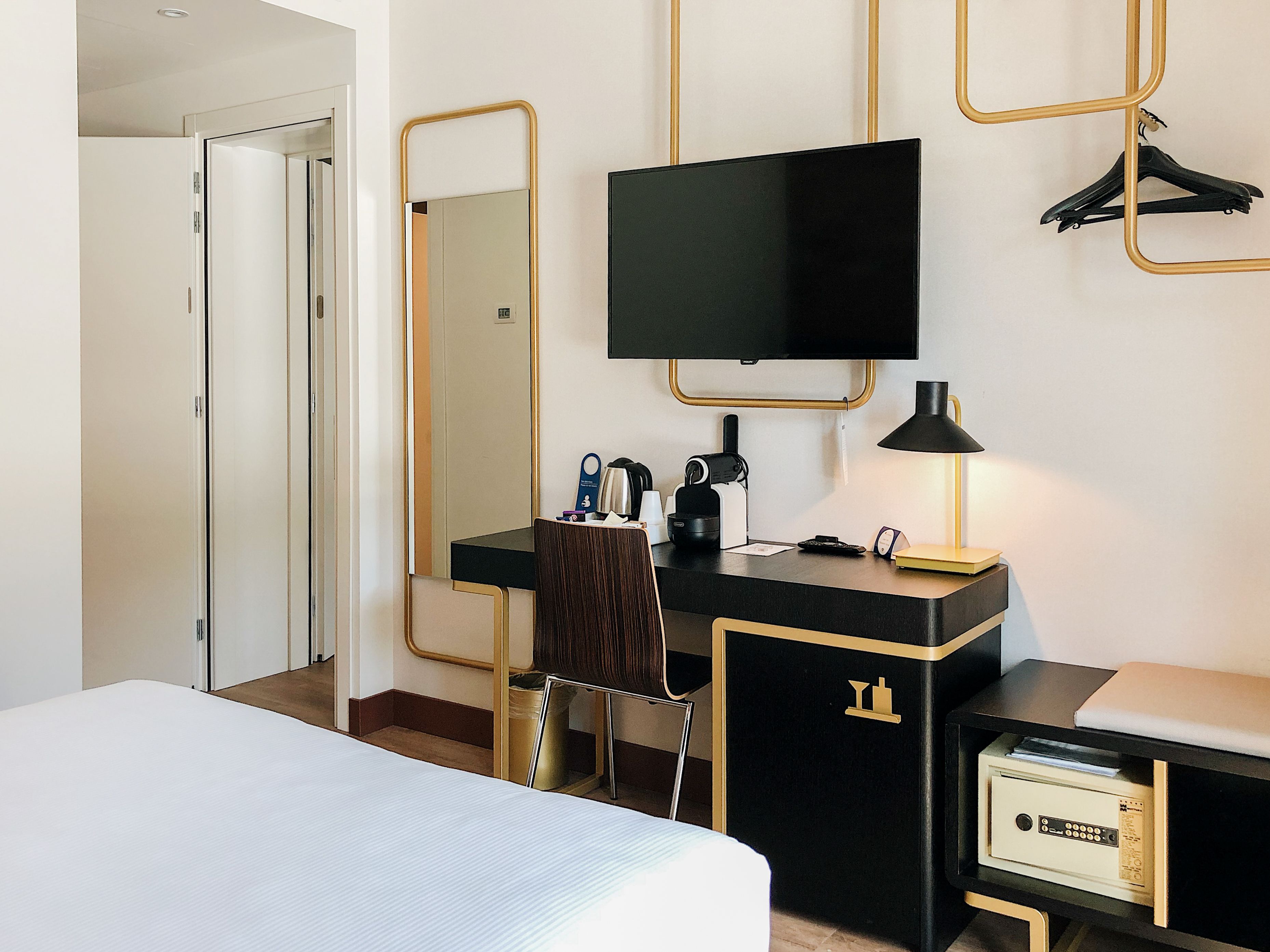 Una habitación de hotel con cama, escritorio con silla, televisión, lámpara y armario.